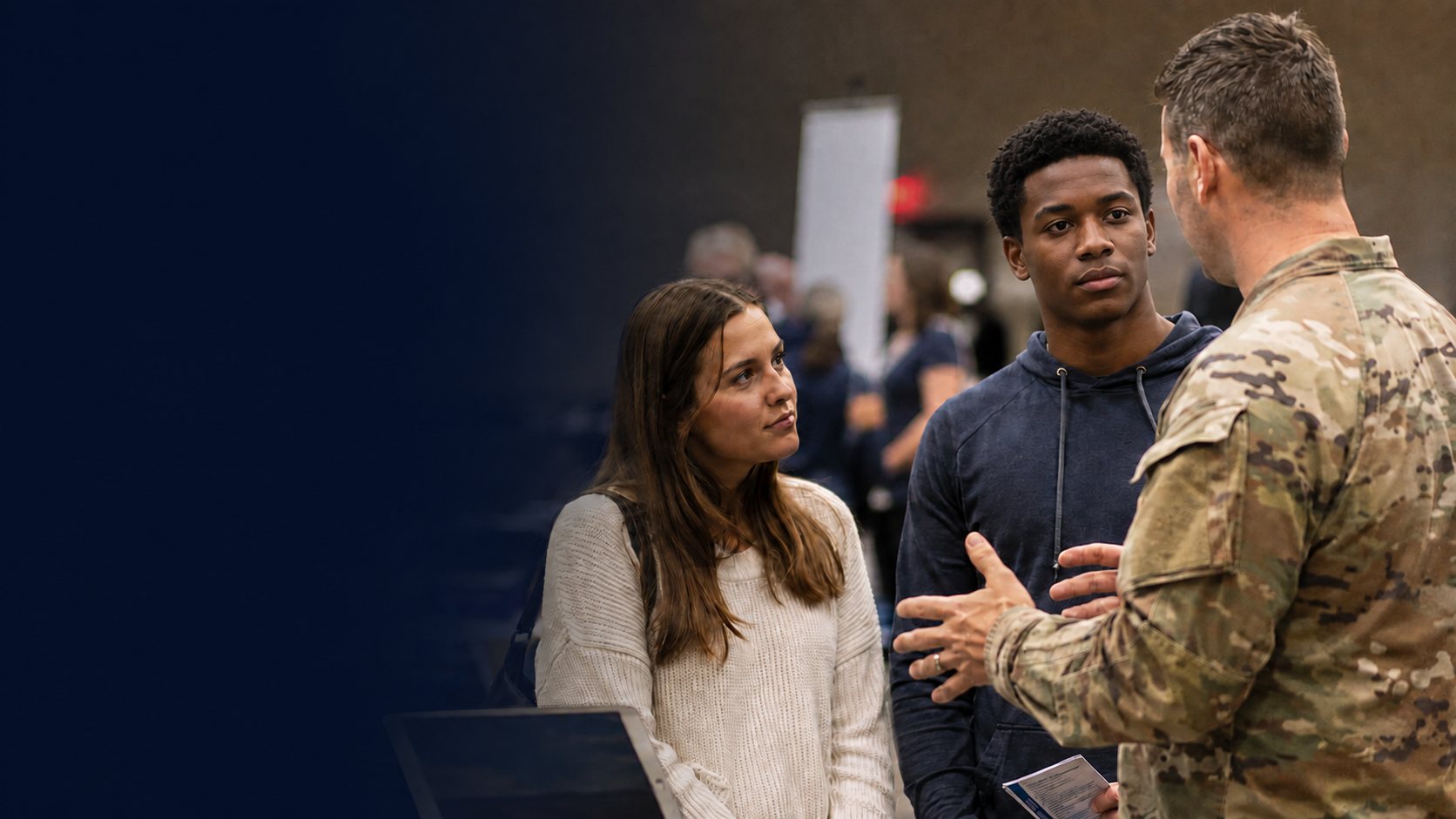 A soldier in uniform speaks with two prospective recruits at an outreach event
